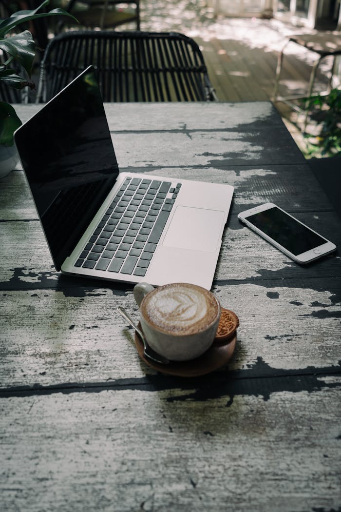 Laptop, smartphone, and coffee cup on a rustic table in an outdoor setting.